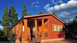 A wooden cabin with a porch, a front door, and a staircase leading to the entrance. - Pinetop | Family Cabin Retreat |  local hikes | 2BR (Pinetop)
