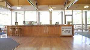 A racquet club activities desk with a wooden counter, chairs, and a view of the outdoors through large windows. - Ramona | Couples Country Retreat | Pool + Tennis (Ramona)