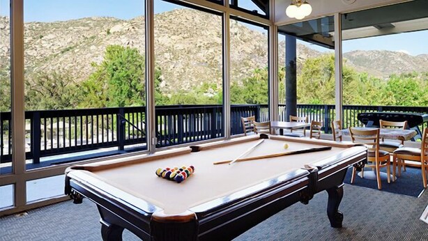 A pool table with balls and a cue stick, surrounded by chairs and tables, with a view of mountains through large windows. - Ramona | Couples Country Retreat | Pool + Tennis (Ramona)