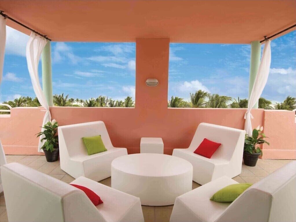 A covered outdoor seating area with white sofas and a round table, surrounded by potted plants.