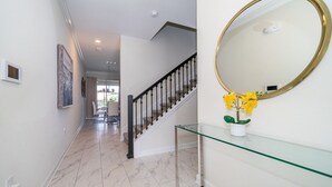En hall med ett marmorgolv, en trappa med svarta räcken och ett glasbord med en vas med blommor.