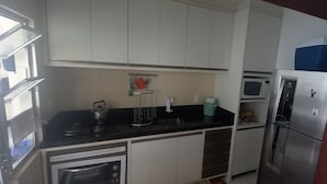 Una cocina compacta con armarios blancos, una encimera negra, un microondas, un refrigerador y un lavamanos pequeño.