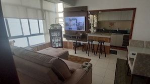 Una sala de estar con sofá, televisor, una zona de cocina y una mesa de comedor.