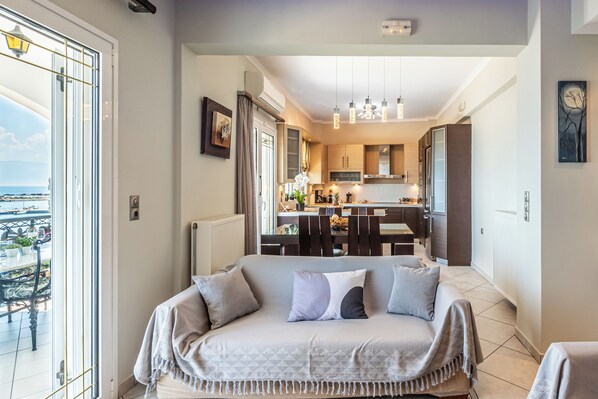 A modern living room with a sofa, a dining area, and a kitchen in the background.
