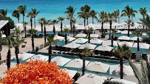 Ein Resort mit Poolbereich, Palmen und Blick auf den Ozean.
