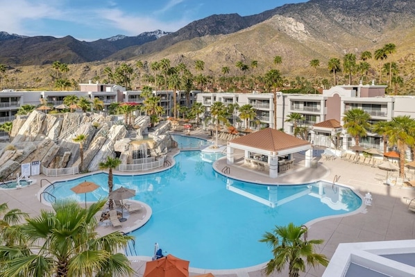 Ein Resort mit großem Pool, Palmen und einer Bergkulisse im Hintergrund.