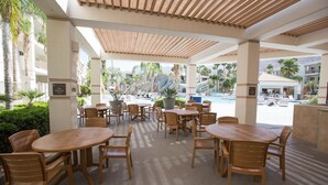 Un espacio al aire libre con mesas y sillas redondas, piscina y palmeras.
