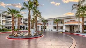 Un hotel con recepción, palmeras y un patio empedrado.