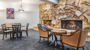 Une pièce avec une cheminée en pierre, une table à manger avec des chaises et une affiche accrochée au mur.