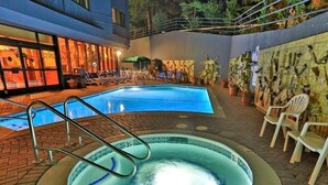Un bain à remous entouré de chaises longues et un espace aménagé au bord de la piscine, avec un sol en briques et un mur décoré de pierres et de plantes.