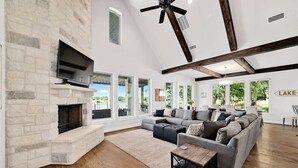 Amplia sala de estar con chimenea de piedra, un sofá seccional gris grande y una mesa de centro de madera.