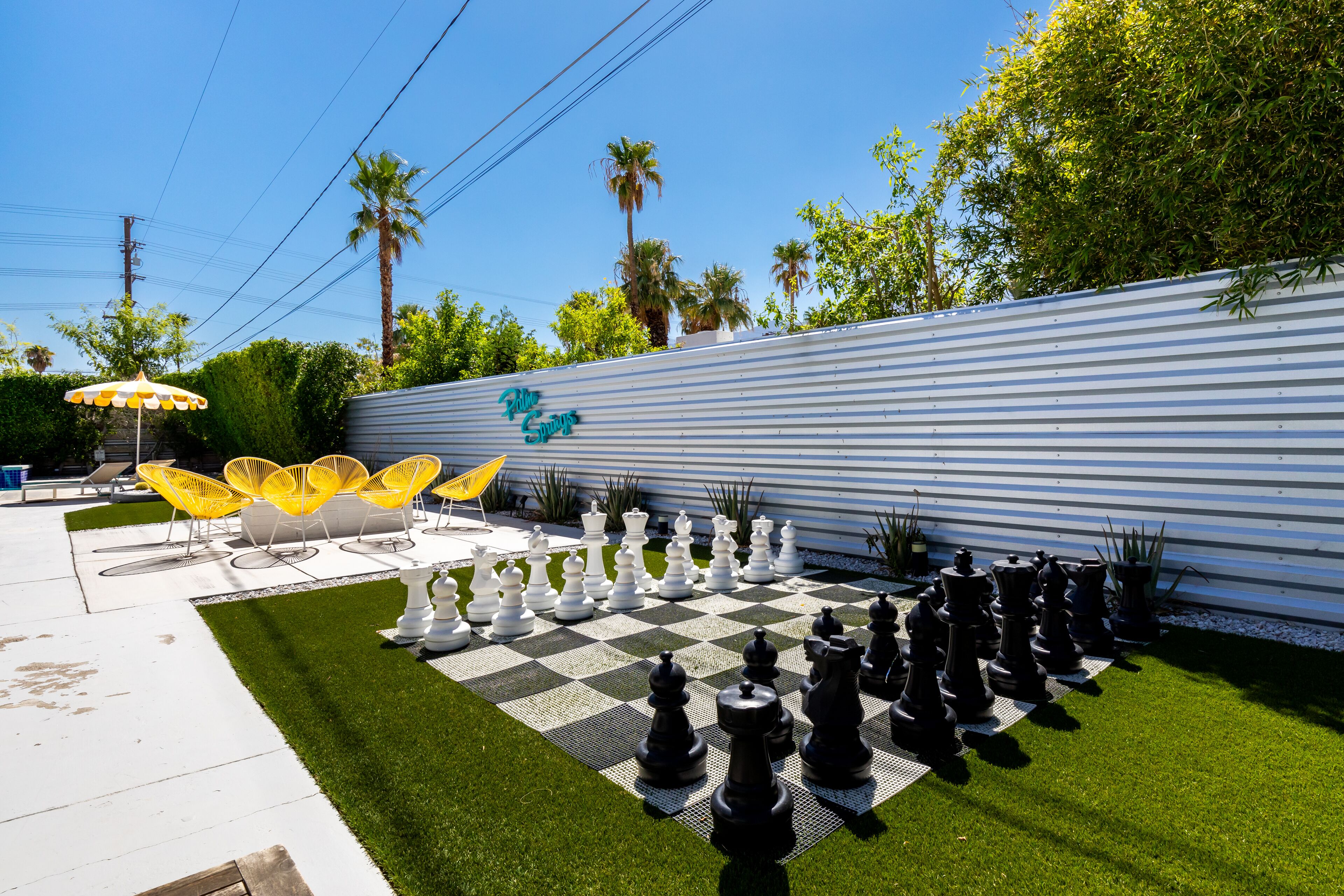 Un jeu d’échecs installé sur une pelouse artificielle, avec un mur métallique en arrière-plan.
