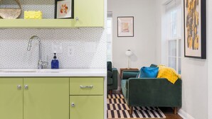 A modern kitchen with green cabinets, a white countertop, and a hexagonal tile backsplash. - Modern Cottage by Hospital, King Bed / Glass Shower (Joplin)