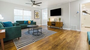 A modern living room with a green sofa, a coffee table, and a flat-screen TV mounted on the wall. - Modern Cottage by Hospital, King Bed / Glass Shower (Joplin)