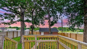 A wooden deck with a view of a brick building and trees in the background. - Modern Cottage by Hospital, King Bed / Glass Shower (Joplin)