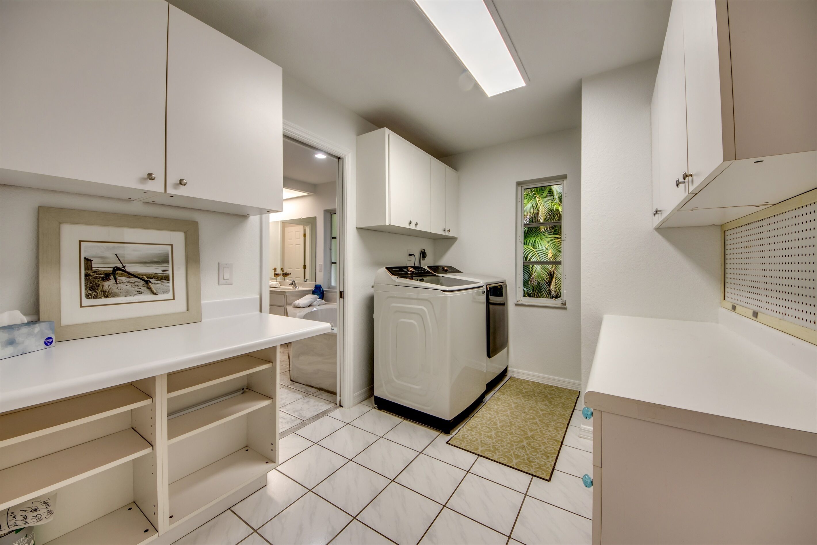 Cocina moderna con muebles blancos, lavadora integrada y ventana con vistas a zonas verdes.