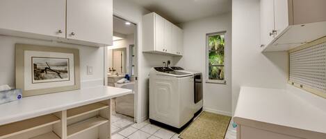 Cocina moderna con muebles blancos, lavadora integrada y ventana con vistas a zonas verdes.