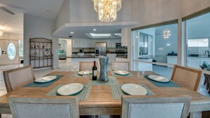 Un espace repas moderne avec une table en bois dressée pour six personnes, entourée de chaises. Un grand vase et une bouteille de vin sont posés sur la table.