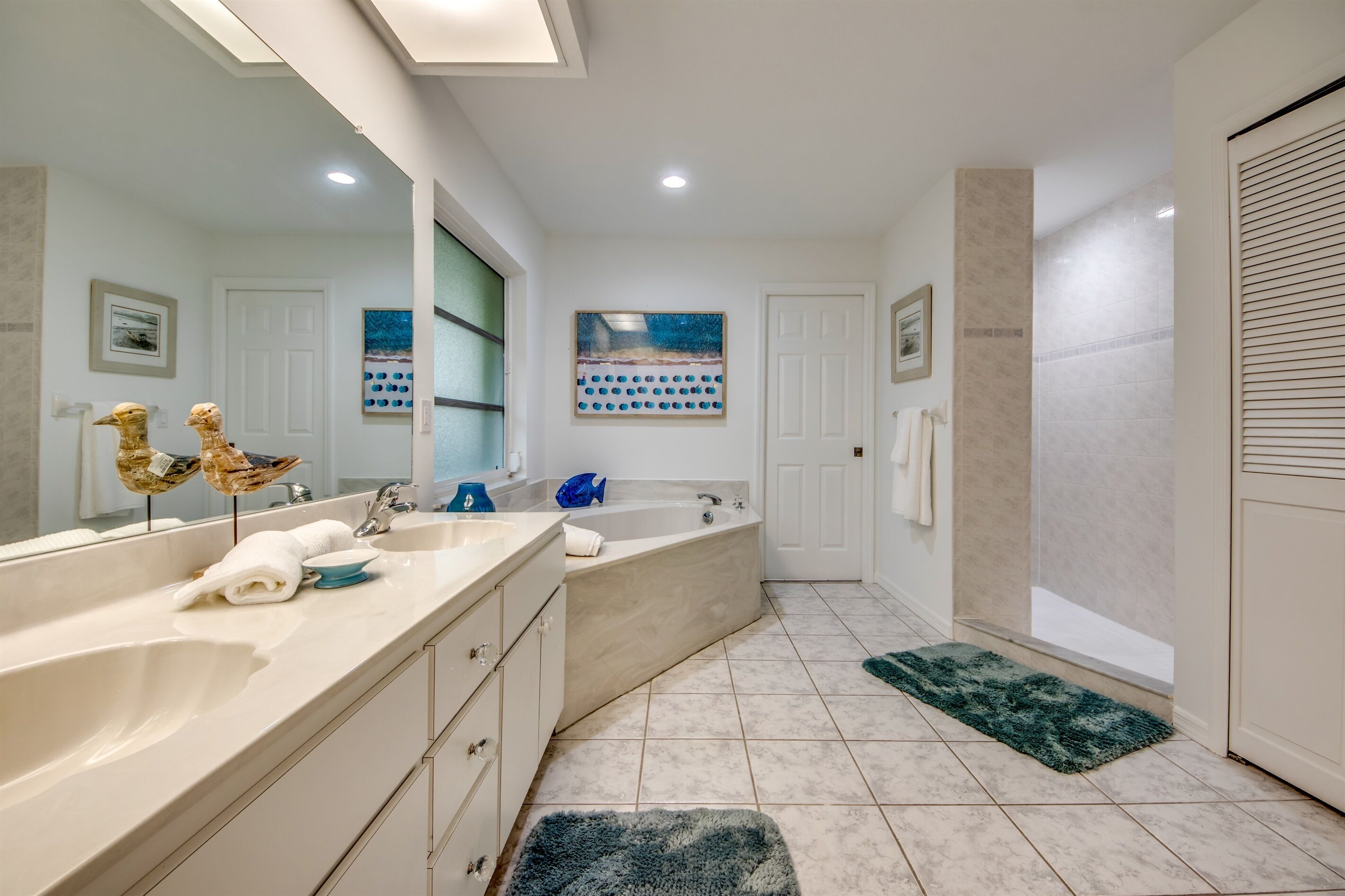 A modern bathroom with two sinks, a bathtub, and a large mirror. There are towels and a rug on the floor.