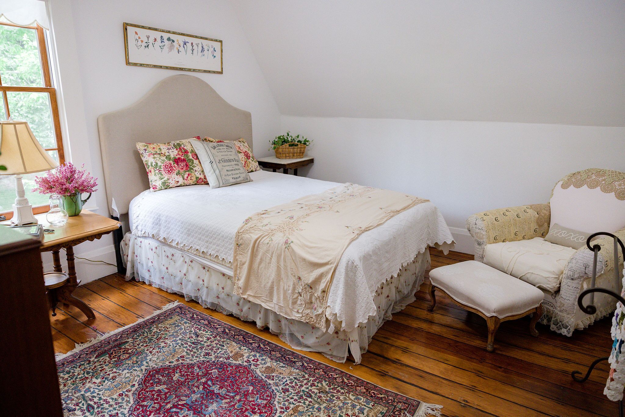 Een slaapkamer met een groot bed, een klein tafeltje met een lamp, een stoel en een vloerkleed.