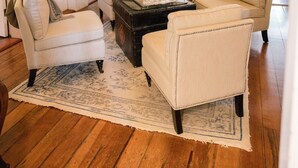 Een woonkamer met een houten vloer, een salontafel en twee witte fauteuils.