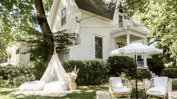 Een wit huis met een veranda, een witte luifel en rieten meubels.
