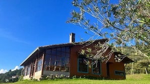 Ein zweigeschossiges Haus mit großen Fenstern und einem Schornstein, umgeben von einer Rasenfläche und Bäumen.