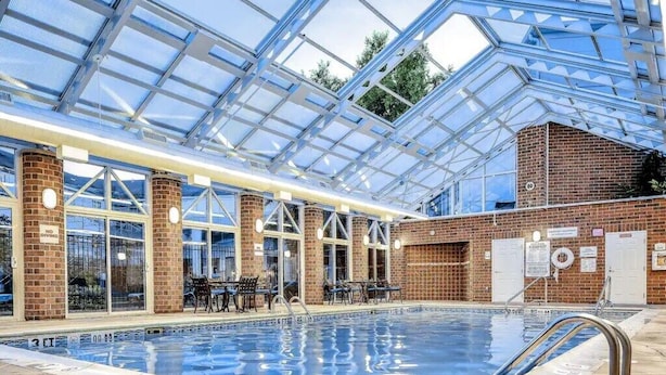 Una piscina interior con techo de cristal, paredes de ladrillo y zona de estar.