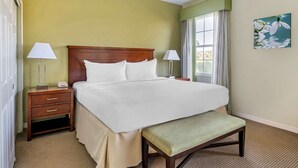 A hotel room with a large bed, two bedside tables with lamps, a bench, and a painting on the wall.