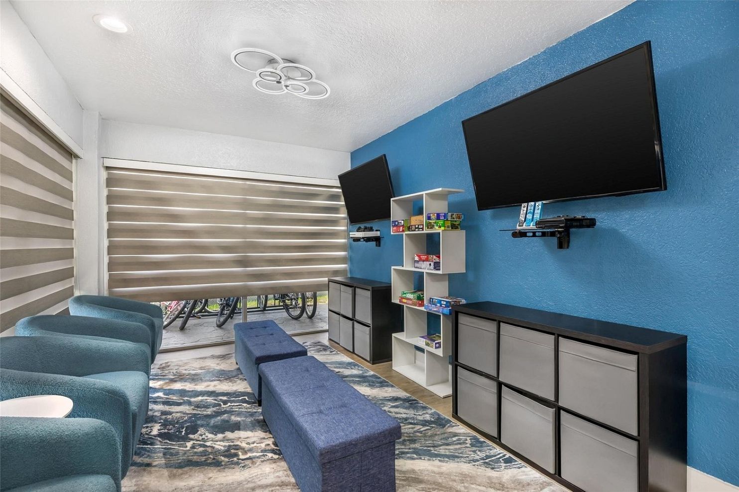 Una sala de estar moderna con televisor de pantalla plana, pared de acento azul, estante empotrado con juegos de mesa y un banco.