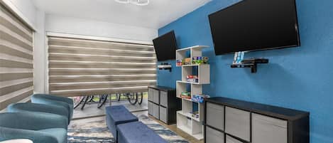 Una sala de estar moderna con televisor de pantalla plana, pared de acento azul, estante empotrado con juegos de mesa y un banco.