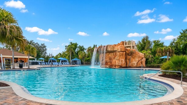 A swimming pool with a waterfall feature, lounge chairs, and palm trees.