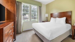 A hotel room with a large bed, a wooden wardrobe, a desk with a lamp, and a window with curtains.