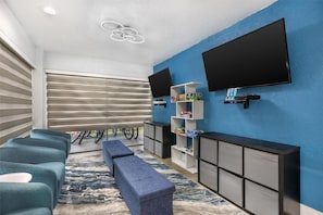 Una sala de estar moderna con televisor de pantalla plana, pared de acento azul, estante empotrado con juegos de mesa y un banco.