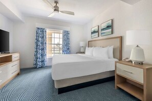 Una habitación de hotel con cama, escritorio, lámpara, televisor y ventana con cortinas.