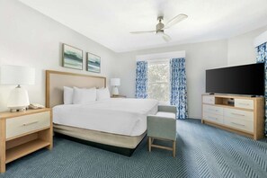 Habitación de hotel con cama, mesitas de noche, televisor, sillón y ventana con cortinas.