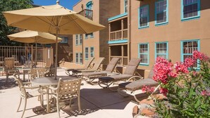 A patio with lounge chairs and umbrellas, a pool, and a building with balconies.