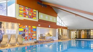 A large indoor swimming pool with clear blue water, a sunroof, and a modern interior design. - Schladming | Friends Alpine Stay | Pool + Spa | 2BR Condo (Schladming)
