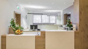 A modern reception area with a wooden reception desk, a computer, and a window with sheer curtains. - Schladming | Friends Alpine Stay | Pool + Spa | 2BR Condo (Schladming)