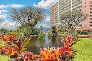 A hotel with a large building, a pond, and tropical plants.