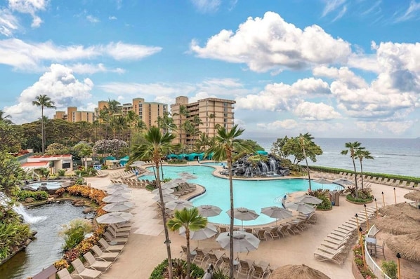 A resort with a large pool, palm trees, and a view of the ocean.