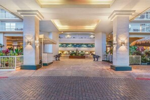 A spacious lobby with a central reception desk, multiple floors visible, and a tropical plant display.
