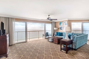 A hotel room with a balcony, a sofa, a coffee table, a TV, and a ceiling fan.