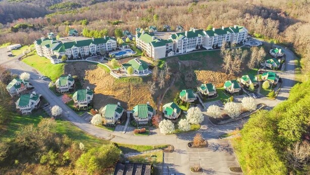 Een resort met meerdere gebouwen, een parkeerplaats en een omliggend bebost landschap.