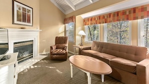 Een woonkamer met een open haard, een bruine leren fauteuil, een beige bank en een kleine tafel.