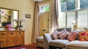 A living room with a sofa, a wooden cabinet, a rug, and a window with curtains. - 3 bedroom accommodation in Skipton (Skipton)