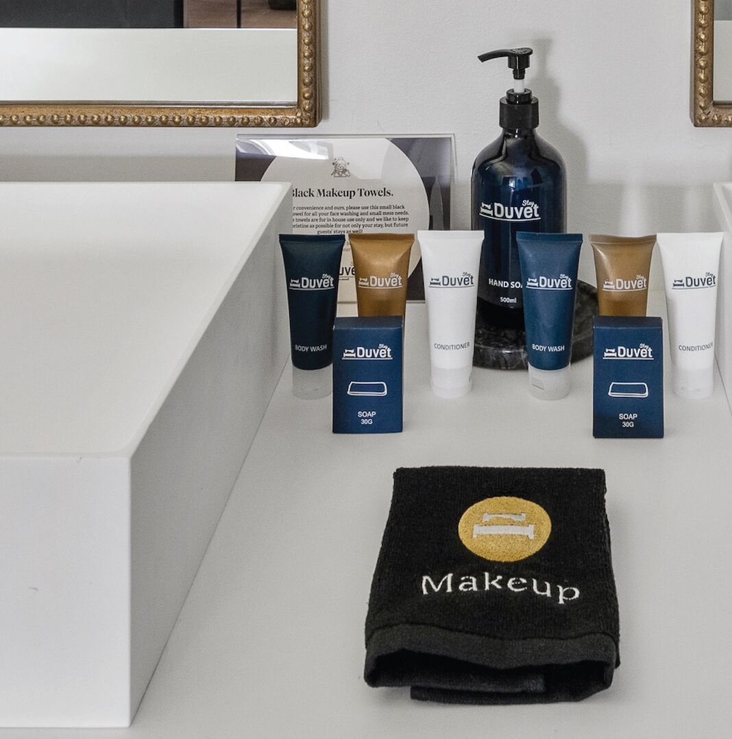 Un meuble-lavabo de salle de bain avec des serviettes noires pour le maquillage, un gel douche, un après-shampoing et un distributeur de savon.