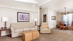 Ein Hotelzimmer mit Sofa, Sessel, Hocker, Esstisch mit Stühlen und einer Chandelier.