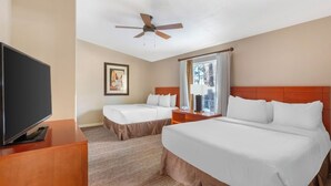 Ein Hotelzimmer mit Bett, Fernseher, Deckenventilator, Gemälde und einem Fenster mit Vorhängen.