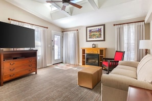 A living room with a flat-screen TV, wooden entertainment center, beige sofa, red chair, fireplace, and a ceiling fan.